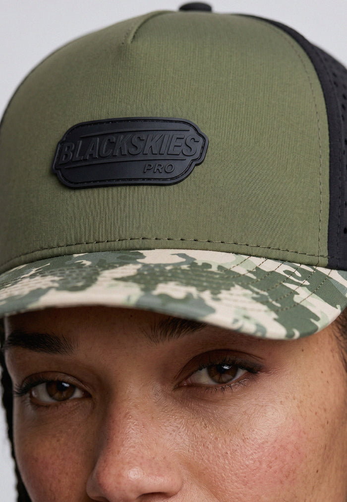 Close-up of a person wearing a green and camouflage cap with a Blackskies logo.