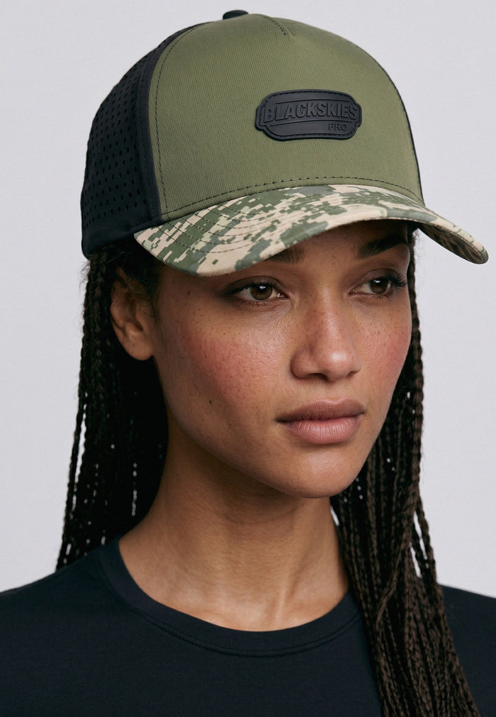 Person wearing a green and black cap with a visible brand logo on a plain background