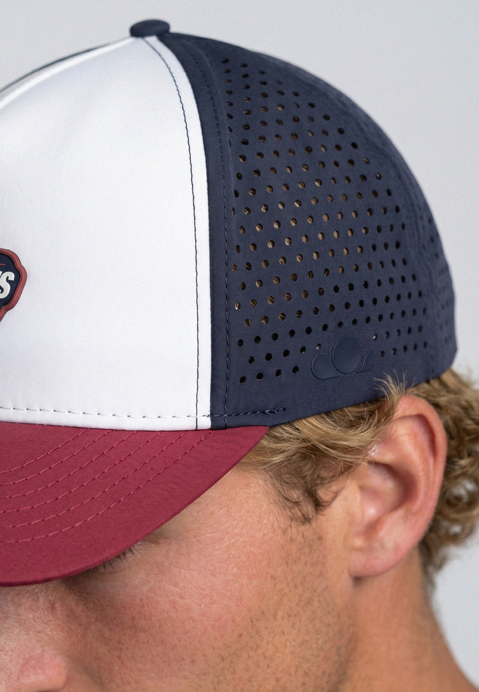 Close-up of a person wearing a baseball cap with white front, navy back, and red brim.
