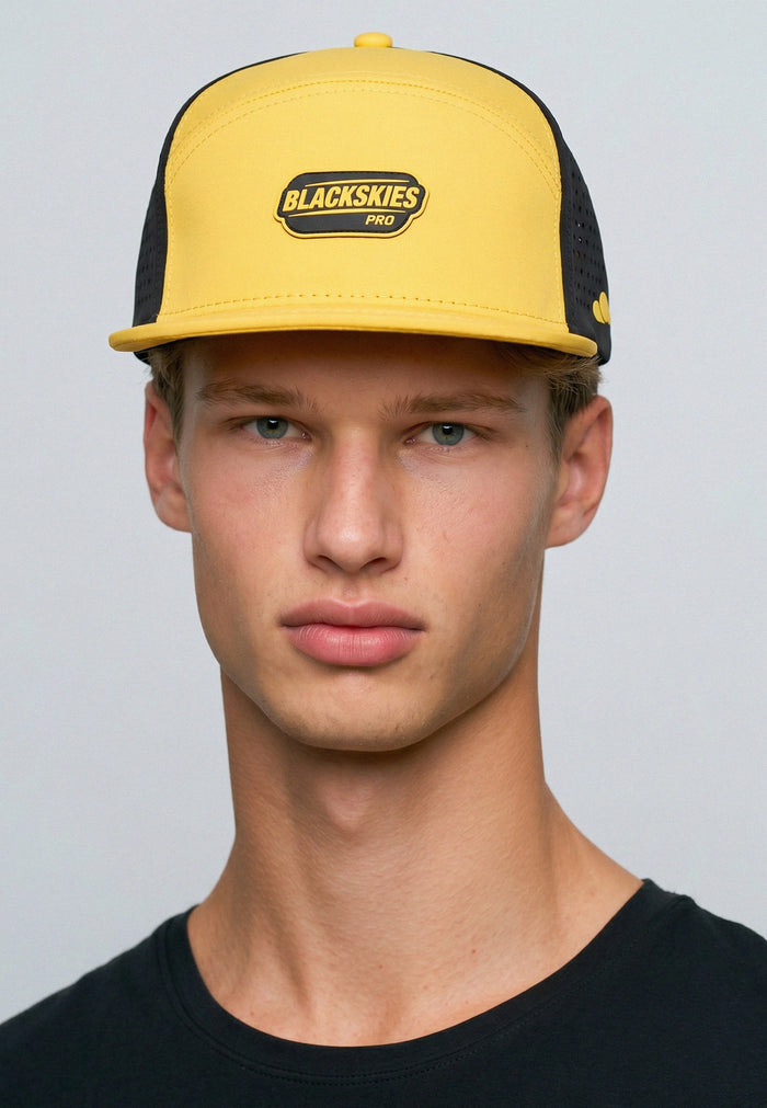 Man wearing a yellow and black cap with 'Blackskies Pro' logo on a gray background