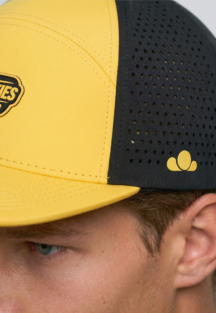 Close-up of a yellow and black cap with a brand logo on a person wearing it.