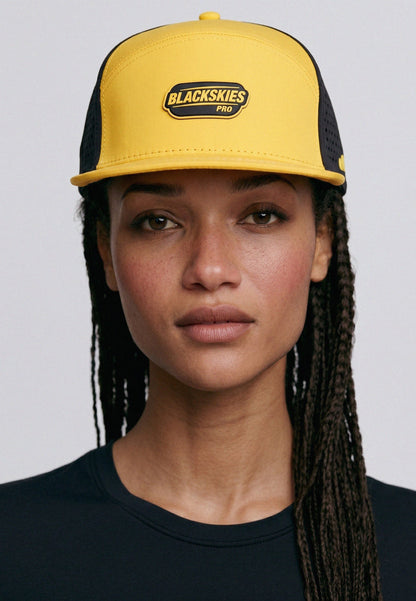 Person wearing a yellow and black cap with 'Blackskies' logo on a gray background