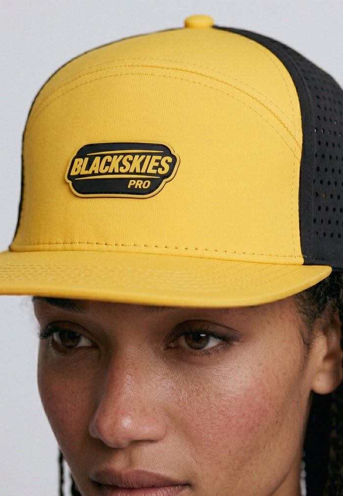 Yellow and black cap with 'Blackskies Pro' logo worn by a person against a gray background