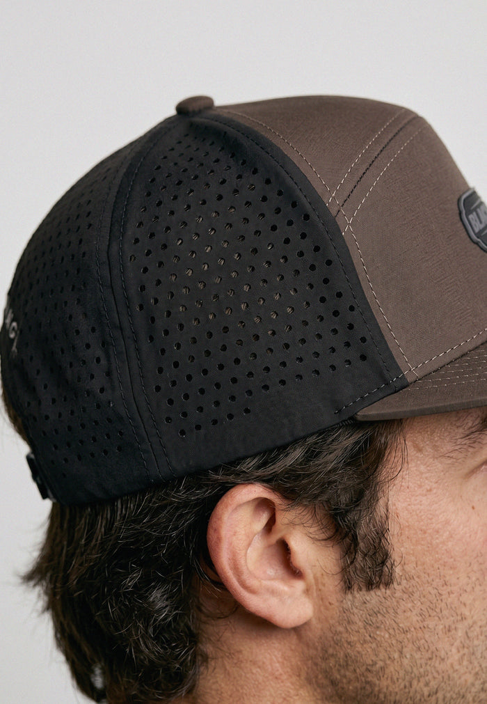 Brown and black baseball cap worn by a person on a light gray background
