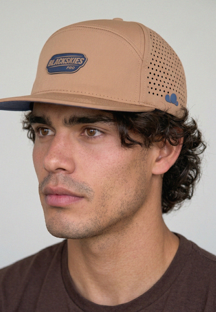 Man wearing a tan baseball cap with a visible brand logo on a plain background
