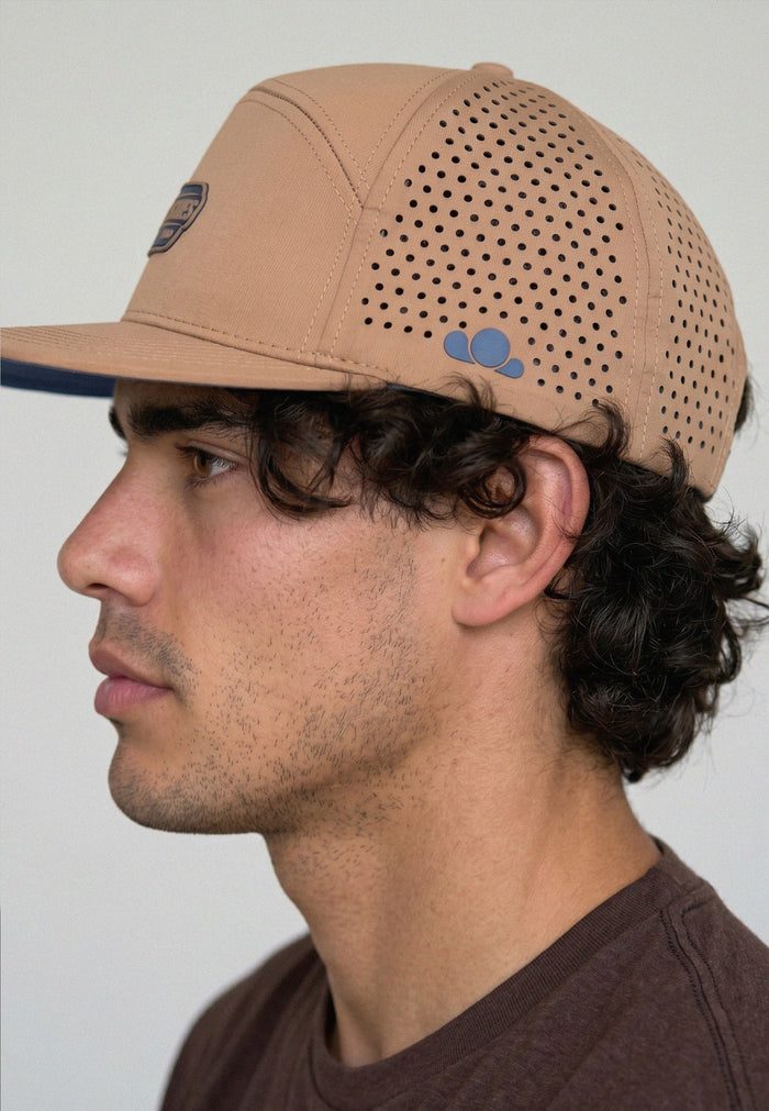 Man wearing a beige cap with a perforated design on a plain background