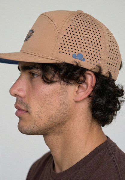 Man wearing a beige cap with a perforated design on a plain background