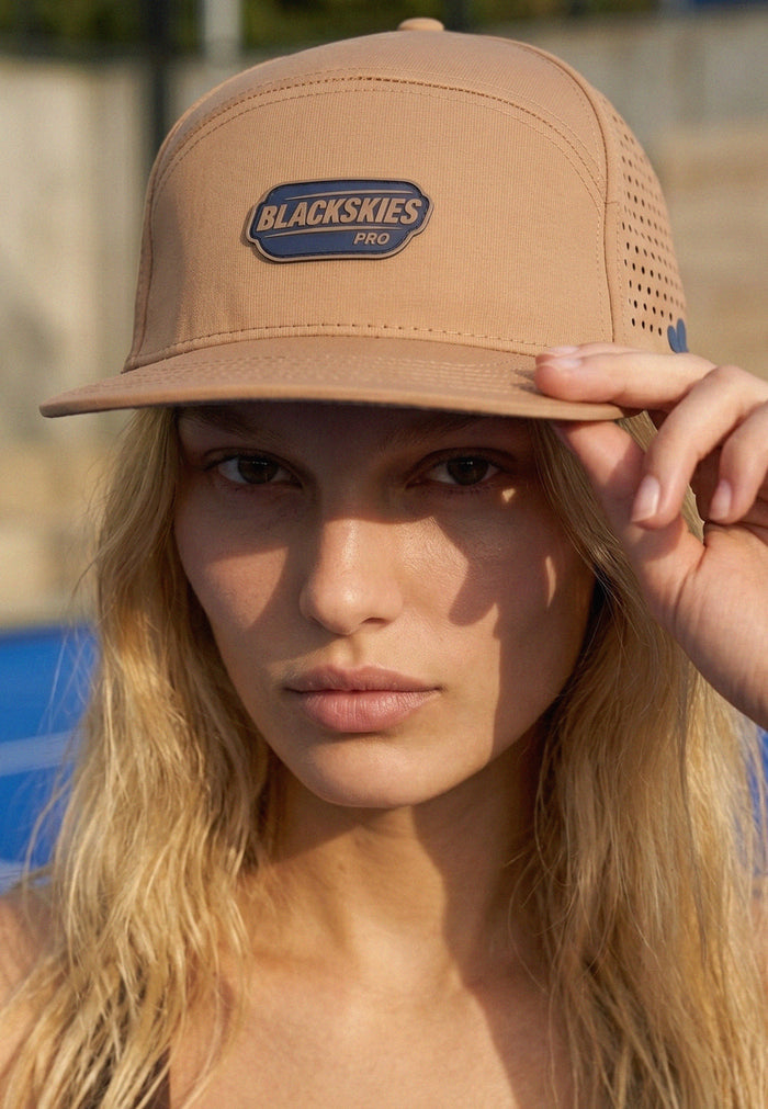 Woman wearing a tan cap with 'Blackskies Pro' logo, outdoors.