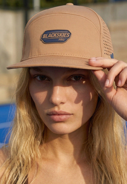 Woman wearing a tan cap with 'Blackskies Pro' logo, outdoors.