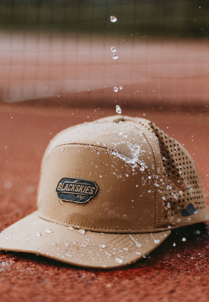 Water repellent sport performance cap in brown with blackskies gum logo on tennis court
