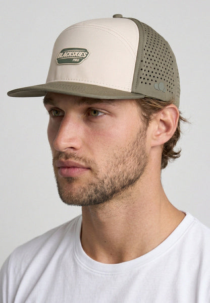 Man wearing a beige and gray cap with a visible brand logo on a plain background
