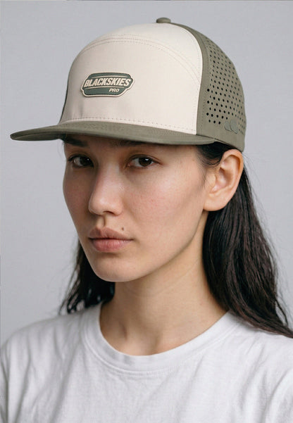 Person wearing a beige and gray cap with a visible brand logo on a plain background