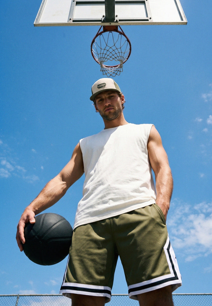 Man holding a basketball under a basketball hoop with a clear blue sky.