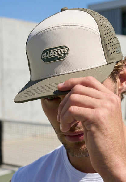 Person wearing a beige and brown trucker hat with 'Blackskies' logo, outdoors.