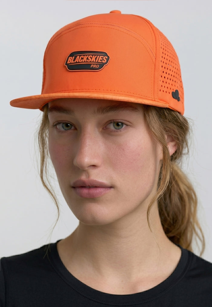 Person wearing an orange cap with a visible brand logo on a plain background