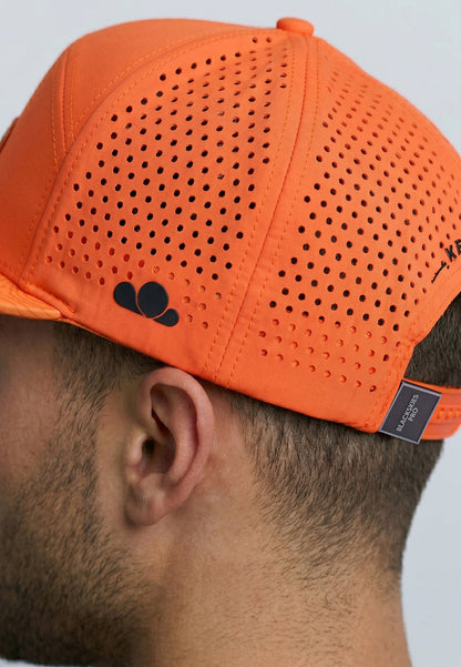 Orange perforated cap worn by a person on a light gray background
