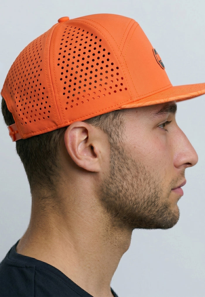 Man wearing an orange perforated cap against a plain background