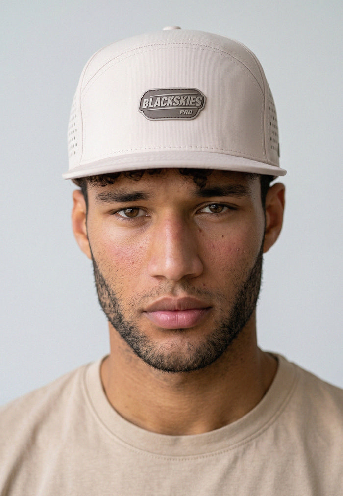 Man wearing a beige cap with a brand logo on a plain background