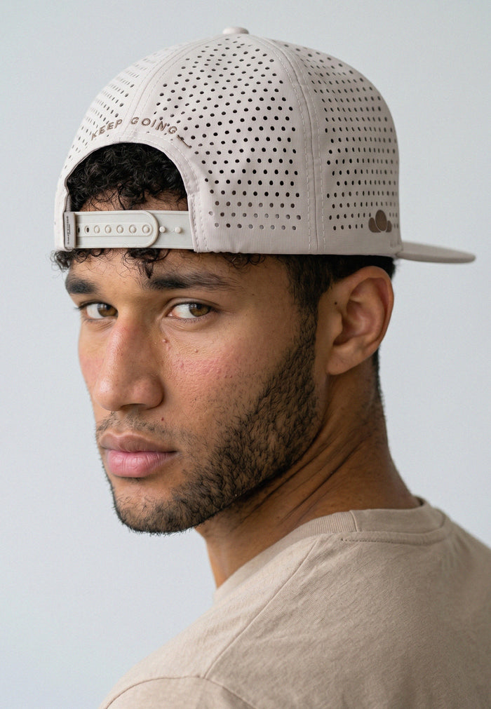 Man wearing a beige cap with a white perforated design on a light gray background