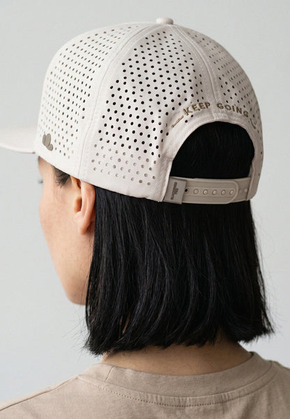 Person wearing a beige cap with 'Keep Going' text on a plain background