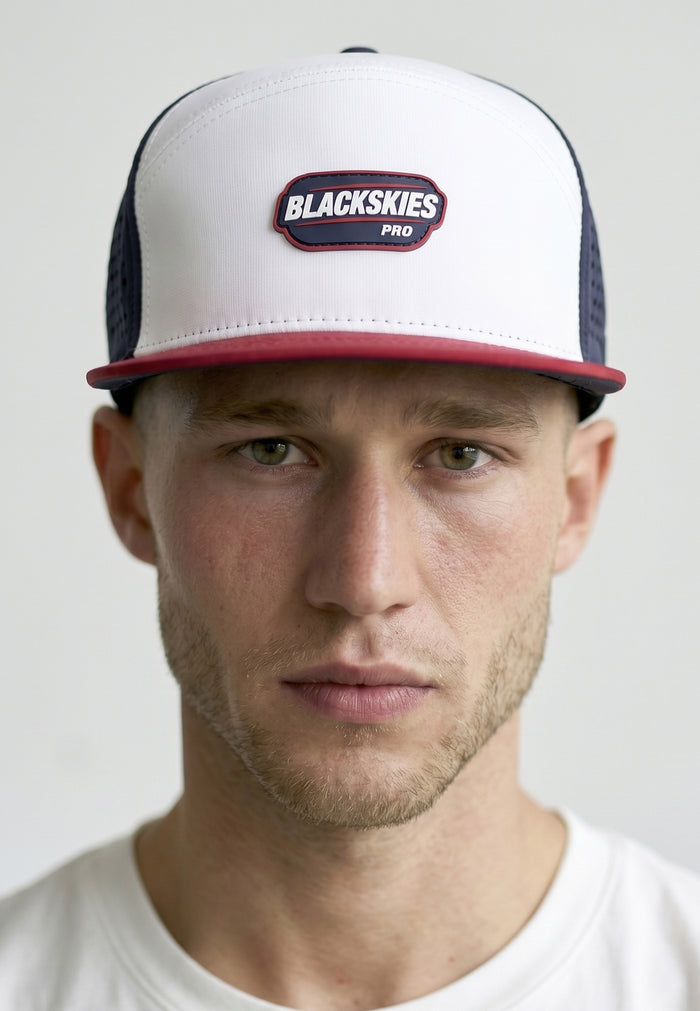Man wearing a white and navy cap with 'Blackskies Pro' logo on a light gray background