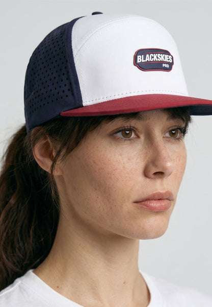 Person wearing a white, navy, and red cap with 'Blackskies' logo on a light gray background
