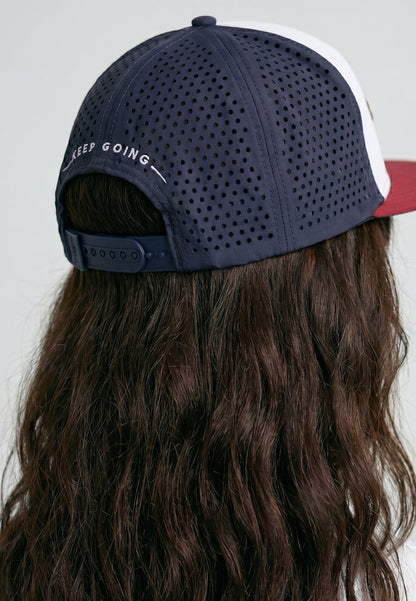 Navy cap with white and red brim worn by a person with long hair on a light gray background