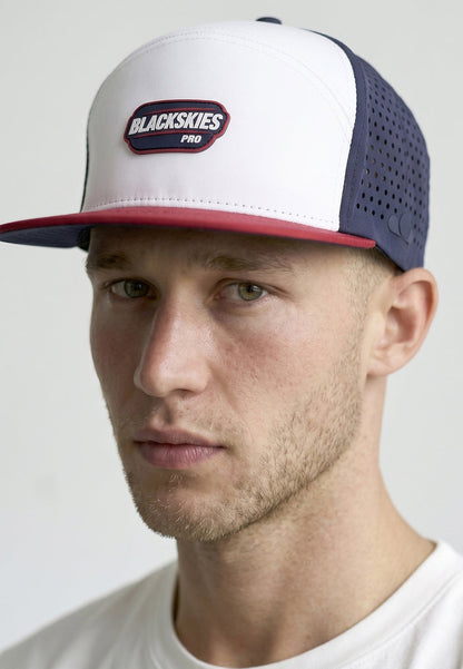 Man wearing a white and navy cap with 'Blackskies Pro' logo on a light gray background