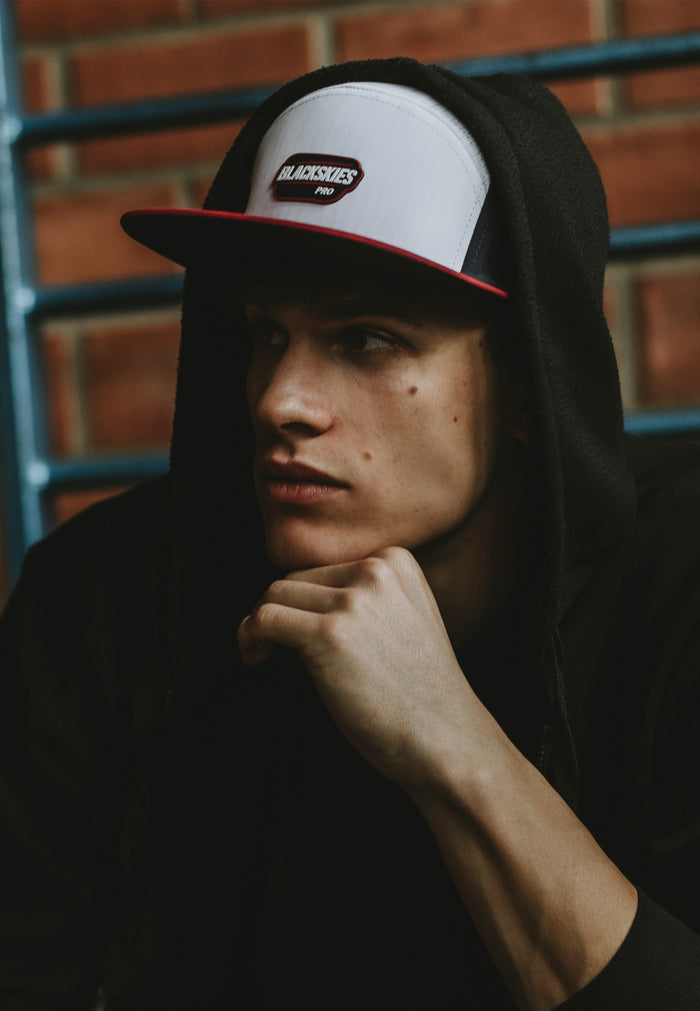 Person wearing a cap with a brand logo against a brick wall.