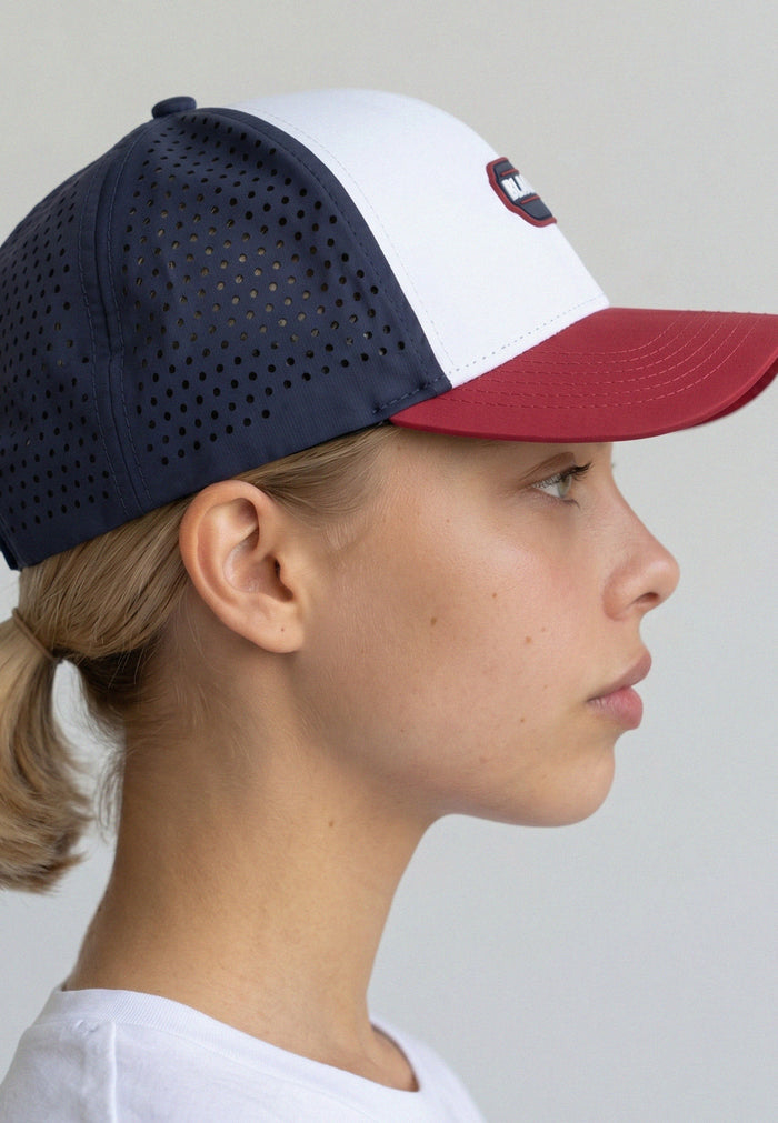 Person wearing a navy and white baseball cap with a red brim on a plain background