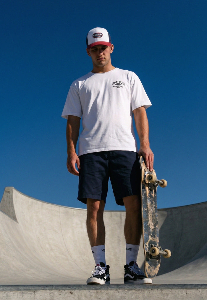 Person holding a skateboard at a skate park with a clear blue sky.