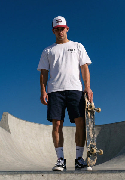 Person holding a skateboard at a skate park with a clear blue sky.