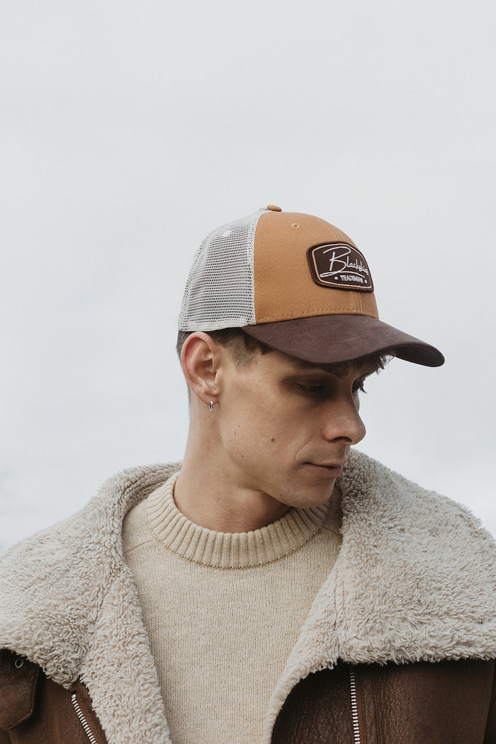 Man wearing a brown and beige cap with a logo against a light background