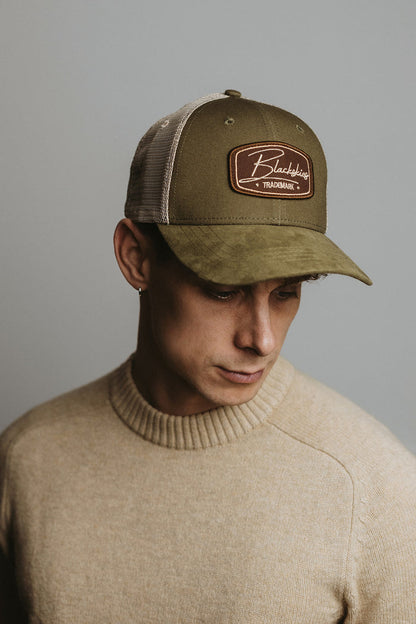 Man wearing a green trucker cap with a logo against a gray background