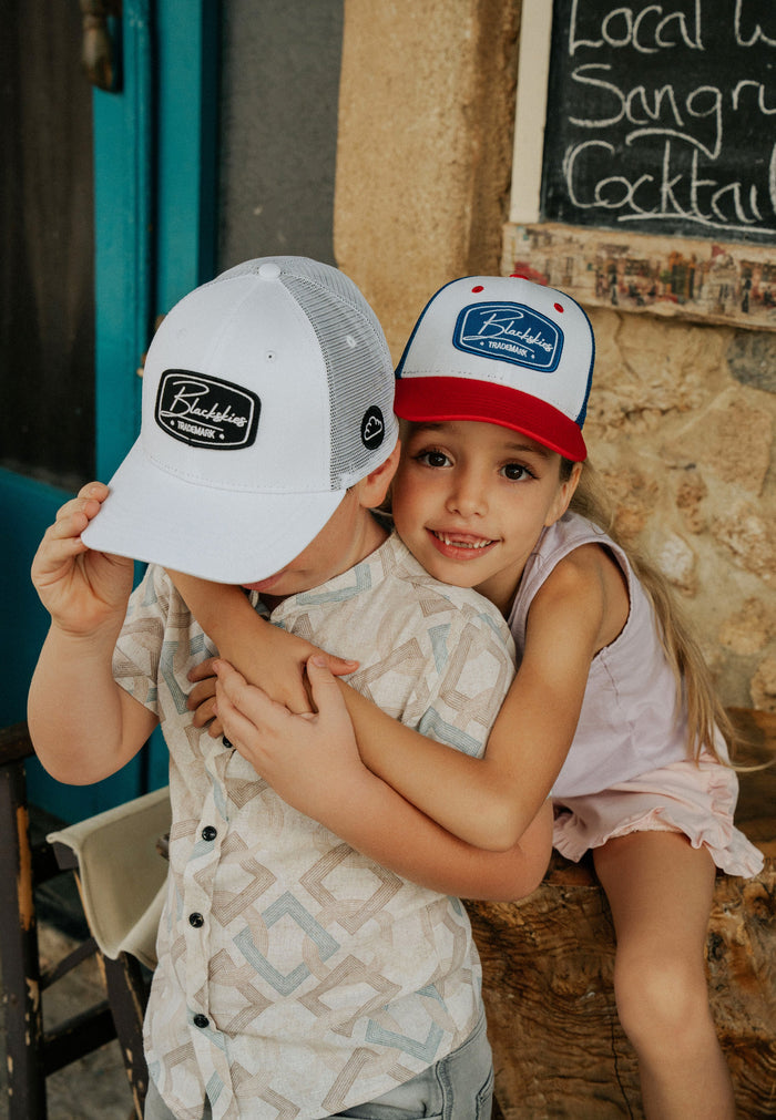 Two children wearing baseball caps in front of a chalkboard sign.