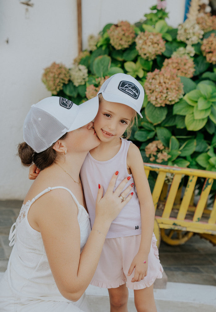 Woman and child wearing matching white caps with a logo, standing in front of flowers.