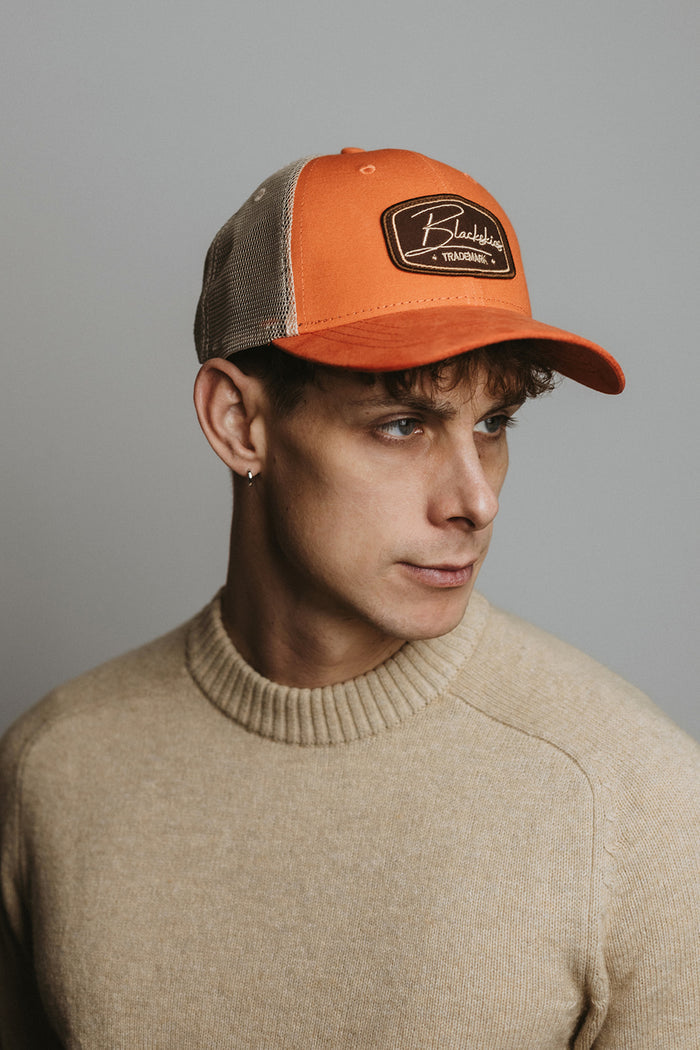 Man wearing an orange and brown cap with a logo against a gray background