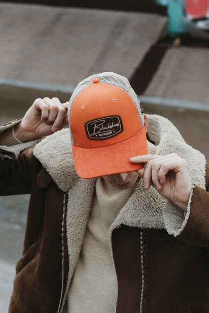 Person holding an orange cap with a logo in front of their face on a wooden surface.