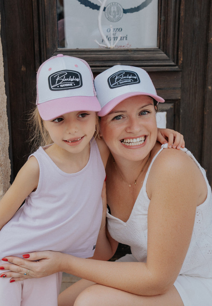 Woman and child wearing matching pink and white caps with a logo, sitting together.