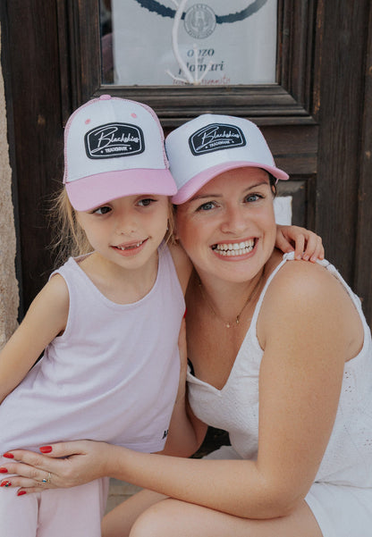 Woman and child wearing matching pink and white caps with a logo, sitting together.