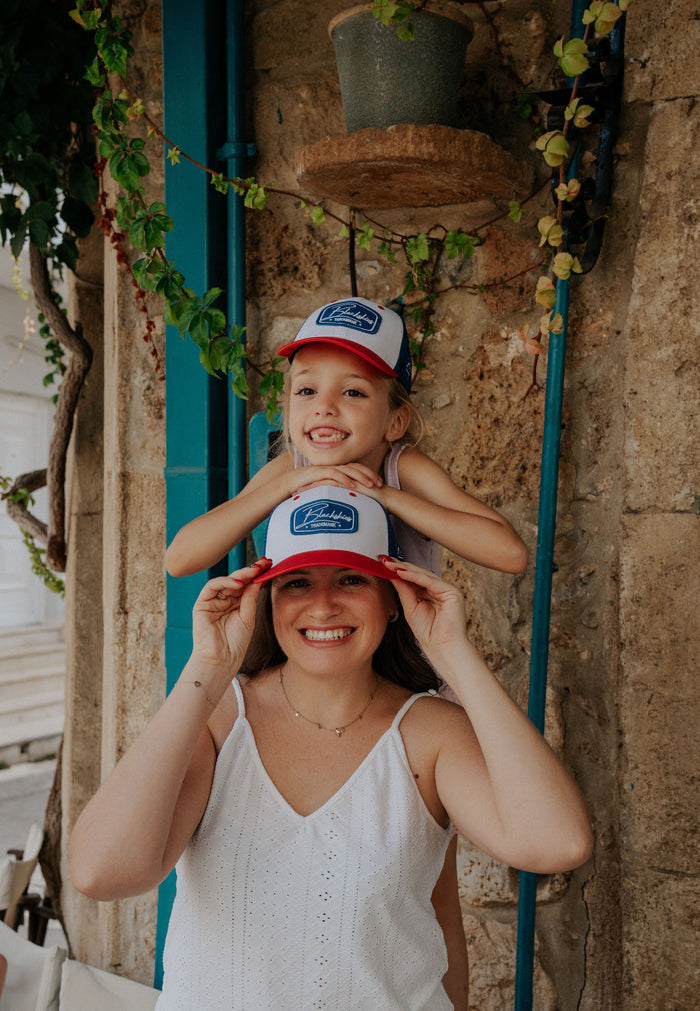 Woman and child wearing matching hats with a logo against a stone wall.