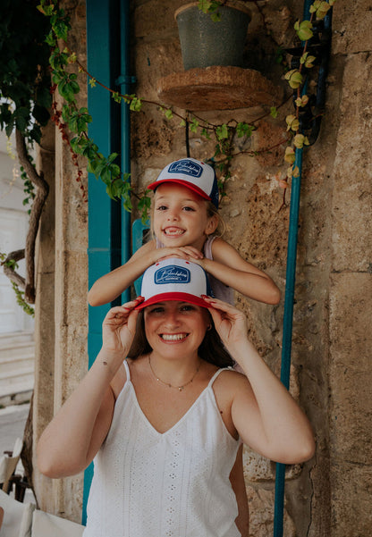 Woman and child wearing matching hats with a logo against a stone wall.