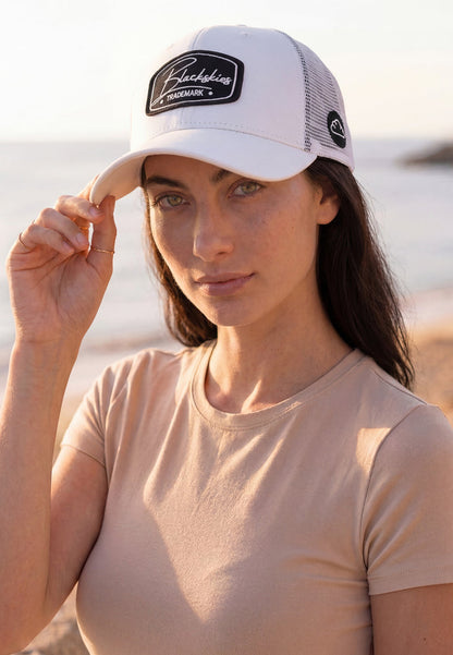 Female model wearing a white Blackskies Race snapback baseball cap with breathable mesh back panels at the beach.