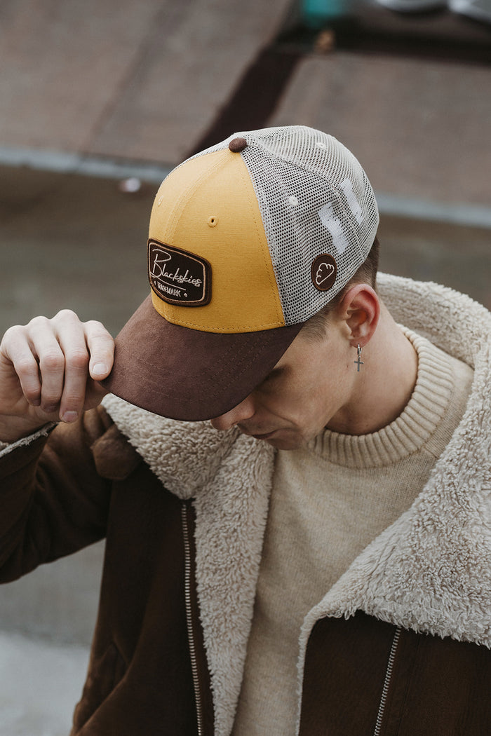 Person wearing a brown and yellow cap with a logo, standing on a wooden floor.