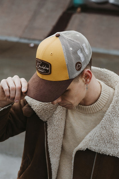Person wearing a brown and yellow cap with a logo, standing on a wooden floor.