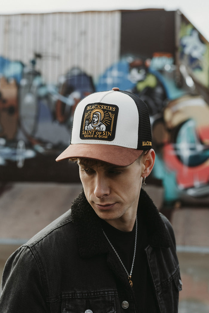 Person wearing a cap with a logo in front of a graffiti wall