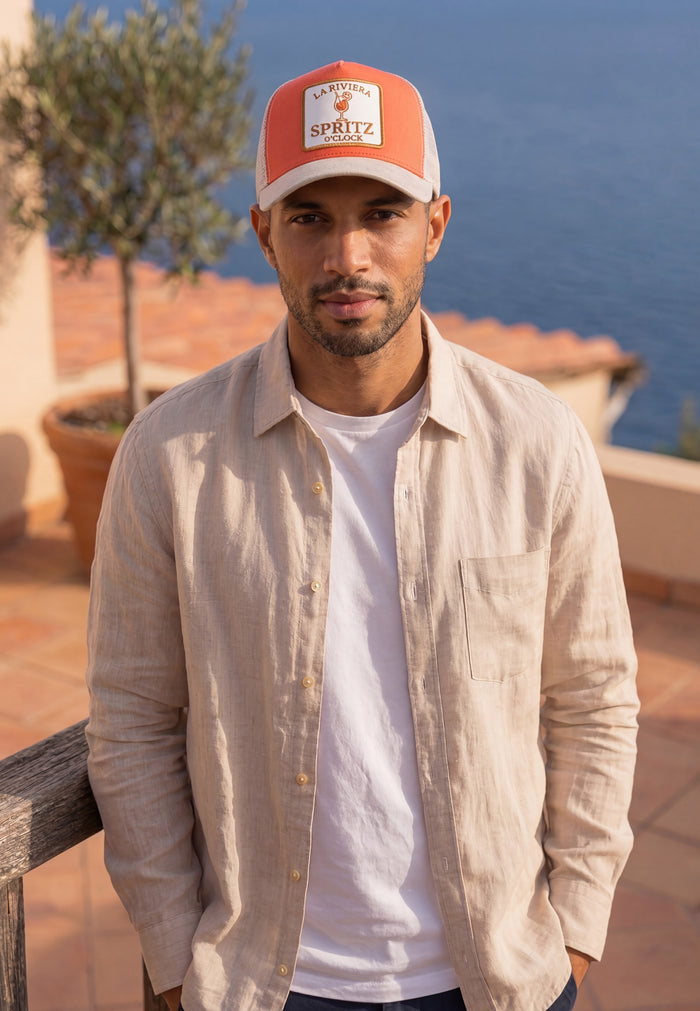 Man wearing a red and white cap with 'Spritz' branding, standing outdoors with a scenic background.