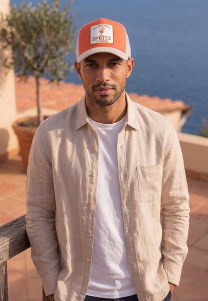 Man wearing a red and white cap with 'Spritz' branding, standing outdoors with a scenic background.