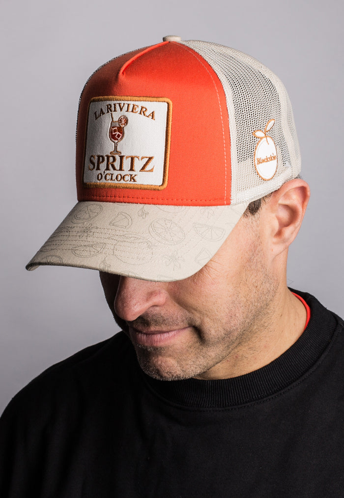 Man wearing a red and beige cap with branding on a gray background